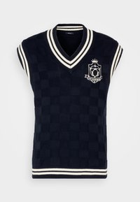 Veste en maille marine à motif écossais, col en V et bordure rayée blanche. Présente un emblème brodé à l'avant.