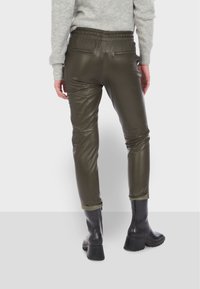 Olivově zelené kalhoty z ekologické kůže s elastickým pasem, zúženými nohavicemi a ohrnutými manžetami, doplněné o černé kotníkové boty.