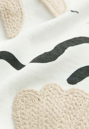 Kangas knit inayonyesha umbo la beige na black juu ya msingi mweupe. Mtindo wa muundo unaonekana kuwa laini na kufuma kwa undani unaonekana.