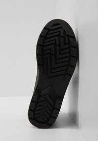 Suela de zapato negro de goma con un patrón de relieve en zigzag, que incluye un logotipo moldeado y la impresión de la talla. Diseñada para tracción y durabilidad.