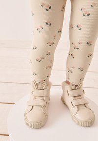 Beige toddler shoes with rabbit ear accents and fur trim, featuring two Velcro straps. Ribbed cream leggings with small floral pattern.