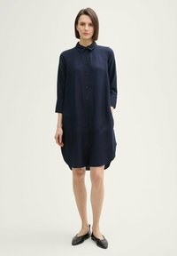 Rochie bleu marin, cu nasturi, cu guler, mâneci până la trei sferturi, buzunare laterale și un tiv ușor curbat. Fabricată dintr-un material ușor, cu o textură netedă.