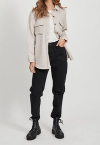 Lys beige knap-UP skjorte med to brystlommer, sorte højtaljede bukser og sorte snørebånds kampboots. Glat stof tekstur.