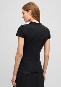 Schwarzes Poloshirt mit kurzen Ärmeln, aus Baumwollmaterial, mit klassischem Kragen und schlankem Schnitt. Glatte Textur, klare Linien.