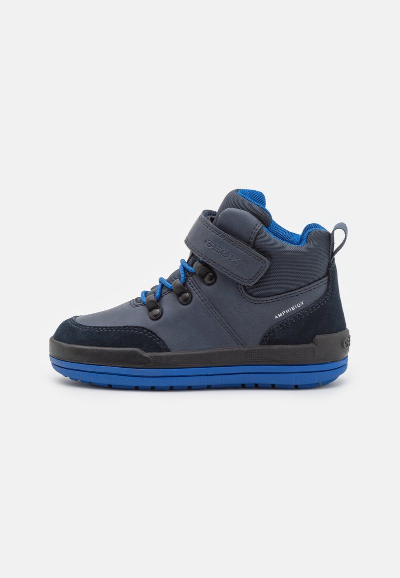 Chaussures montantes bleu et gris avec bride en velcro, matériaux lisses et texturés, bout rond et semelle en caoutchouc avec motif antidérapant.