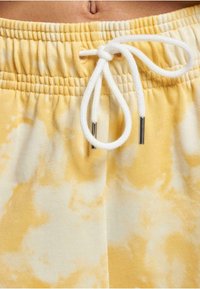Žlté šortky s tie-dye vzorom vyrobené z textúrovanej bavlny, s elastickým pásom a bielym šnúrkou s kovovými koncami.