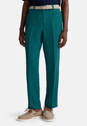 Pantaloni in lino turchese con vestibilità rilassata, caratterizzati da una cintura tessuta beige testurizzata. Abbinati a scarpe da barca marroni chiare e lacci neutri.