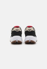 Black and beige athletic shoes with a white sole. Features red accents and embossed branding on the heel. Textured rubber outsole.