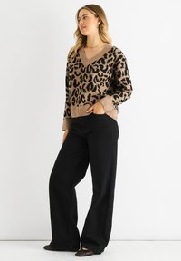 Beige knit sweater with a black leopard print, V-neck design, and ribbed cuffs, paired with black wide-leg pants and black shoes.