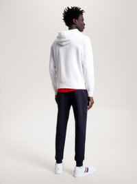 Sweatshirt branco com capuz, camada vermelha por baixo, calças de moletão azul-marinho e ténis brancos com detalhes vermelhos e azuis. Tecido suave, corte relaxado.