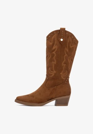 Bota de vaquero de ante marrón con puntera afilada, costuras decorativas y pequeños remaches en la parte superior. Tacón grueso y apilado para mayor estabilidad.