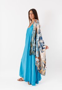 Vestito maxi senza maniche blu con tessuto fluido, abbinato a uno scialle leggero con motivo floreale nei toni beige, blu e verde.