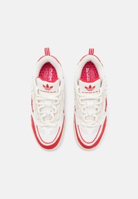White and red athletic shoes featuring a lace-up design, textured sides, the Adidas logo, and a padded collar with a graphic insole.