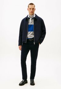 Giacca blu navy con zip, maglione a righe grigio e blu, pantaloni in corduroy blu navy, scarpe in pelle nera. Design semplice, texture liscia, vestibilità sartoriale.