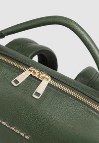 Mochila de cuero verde con acabado texturizado, equipada con una cremallera dorada, dos asas y correas ajustables para opciones de transporte versátiles.