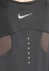 Top atlético negro hecho de tela de malla. Cuenta con un escote redondeado, logo de Nike en gris y puntos decorativos grises a lo largo del frente.