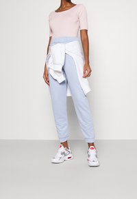 Pink short-sleeve top with logo, light blue sweatpants with elastic waist and cuffs, and white sporty shoes with red and grey accents.