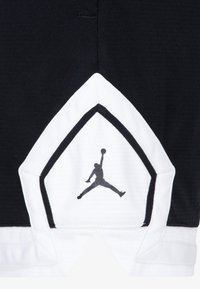 Černé sportovní šortky mají výrazný bílý geometrický vzor na lemu, černé logo Jumpman, strukturovanou tkaninu a kontrastní švy.