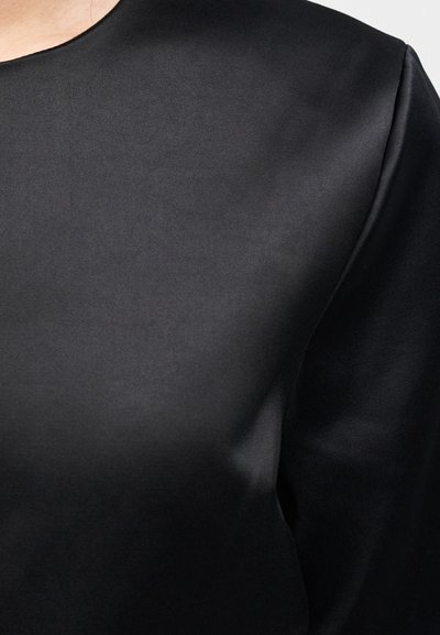 Melnas satīna blūze ar gludu tekstūru, apaļu izgriezumu un viegli strukturētām pleciem, kas izceļ tās eleganto siluetu.
