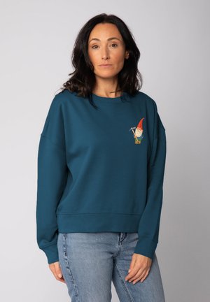 Sweatshirt turquoise à coupe décontractée, col rond et manches longues. Illustration d'un gnome sur le devant. Texture douce, design décontracté.