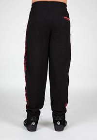 Zwarte textuur joggingsbroek met roze zijkanten en logo. Elastische tailleband met achterzak en een geribbelde onderkant. Gekocht in combinatie met zwarte schoenen.