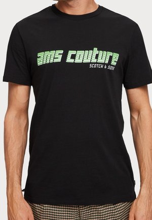 Mężczyzna w czarnej koszulce z zielonym napisem „ams couture” i mniejszym białym napisem „Scotch & Soda” na piersi, widoczny od ramion do bioder.