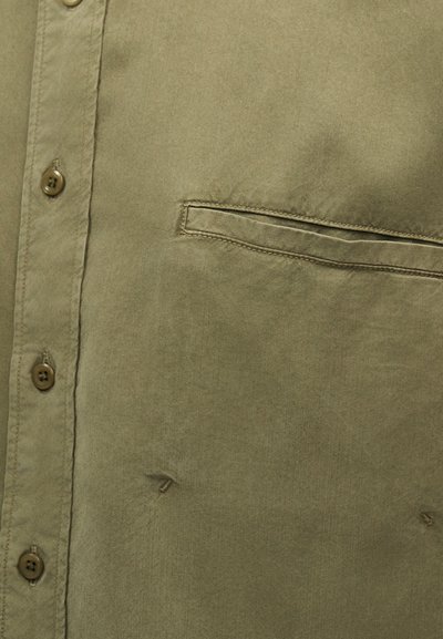 Πουκάμισο χακί με κουμπιά, με ραμμένη τσέπη στο στήθος και εμφανείς ραφές σε υφασμάτινη υφή.