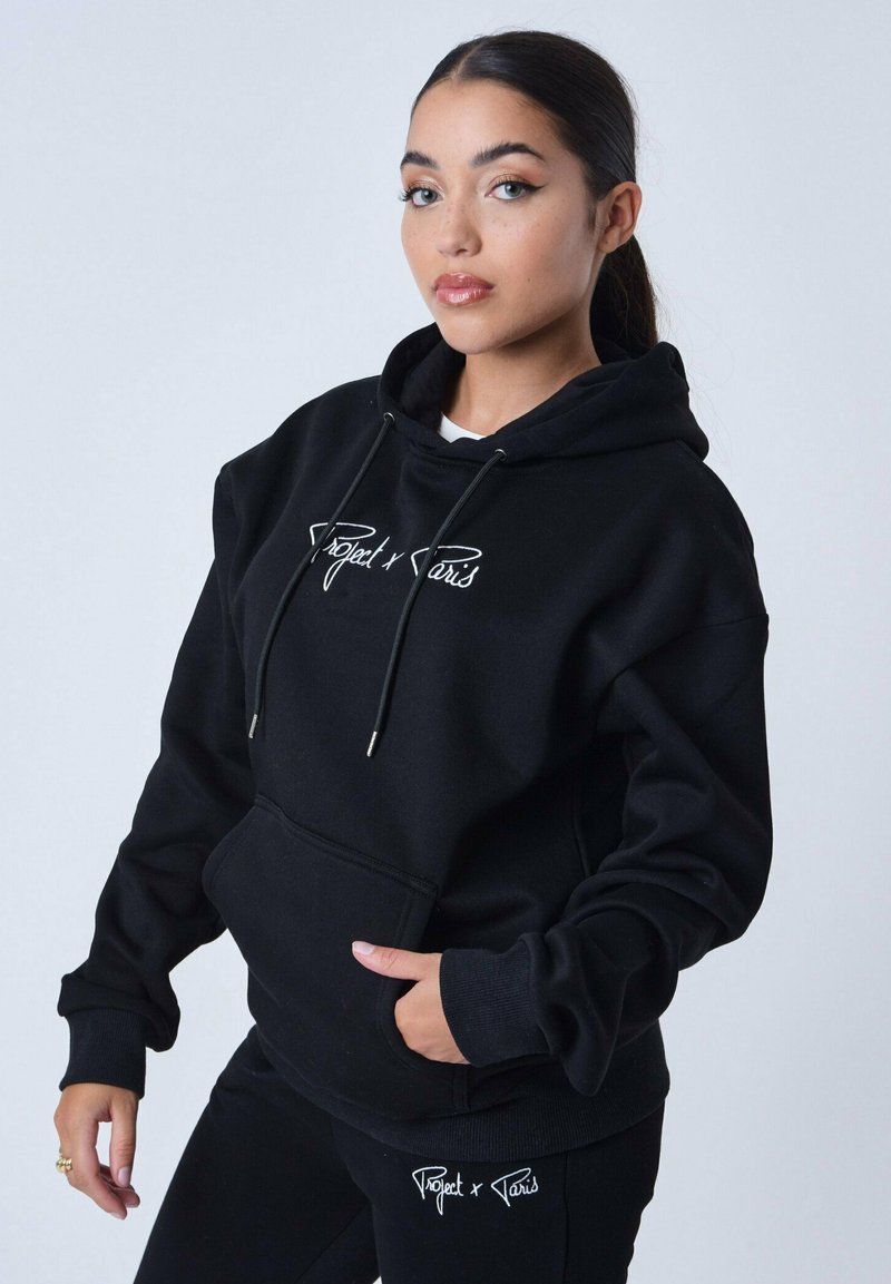 Zwarte hoodie van zacht stof met een kangoeroe pocket, voorzien van witte geborduurde tekst "Project x Paris" op de voorkant en bijpassende zwarte broek.