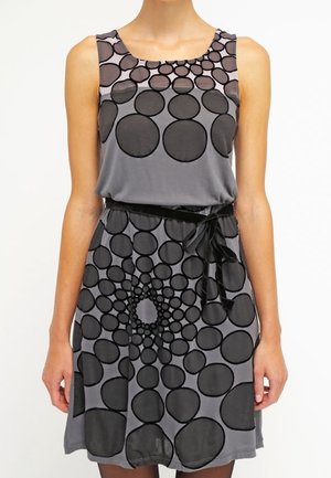 Ärmelloses graues Kleid mit großen und kleinen schwarzen kreisförmigen Mustern und einem schwarzen Band, das in der Taille gebunden ist.