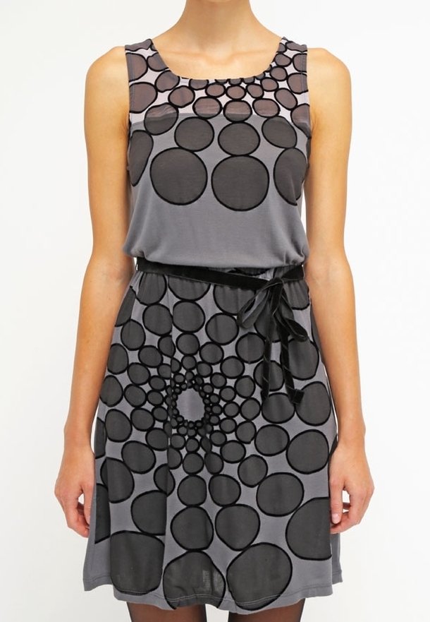 Robe grise sans manches avec de grands et petits motifs circulaires noirs et un ruban noir noué à la taille.