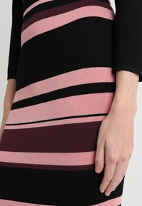 Robe en maille présentant des rayures horizontales noires, roses et bordeaux, avec une silhouette ajustée et une texture lisse.