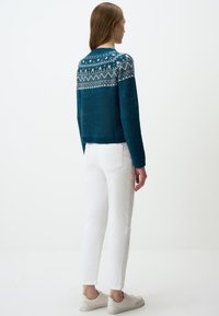 Teal cropped sweater met witte geometrische patronen op de schouders, gecombineerd met witte rechte jeans en lichte sneakers.