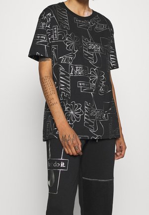 Czarny T-shirt z białymi logo i grafikami Nike, krótkie rękawy, bawełniana tkanina, luźny krój, z różnorodną typografią i kwiatowymi wzorami.
