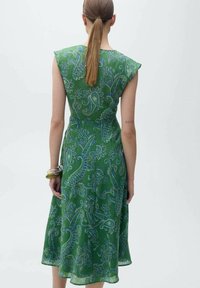 Grünes Kleid mit kurzen Ärmeln, das ein Paisleymuster in Blau und Weiß aufweist. Fließender Stoff mit taillierter Taille und weit ausgestelltem Rock.