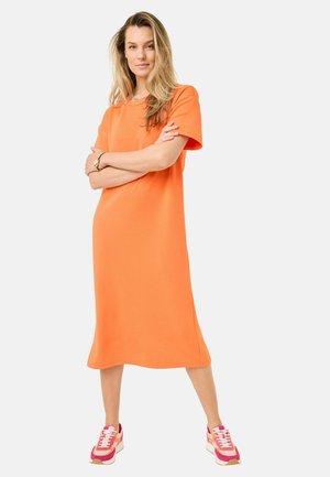 Orange knälång klänning i mjukt tyg, med korta ärmar och avslappnad passform. Bärs med rosa och vita sneakers.