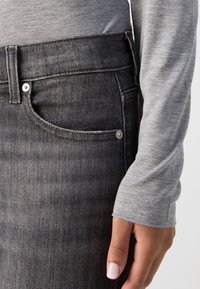 Dunkelgrauer Denim-Rock mit klassischer Passform. Mit Fronttaschen und silberfarbenen Beschlägen, ein weiches graues Langarmoberteil ist teilweise sichtbar.