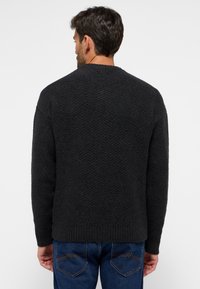 Schwarzer, strukturiert gestrickter Pullover mit Zickzackmuster, Rundhalsausschnitt und Rippensaum, kombiniert mit blauen Jeans.