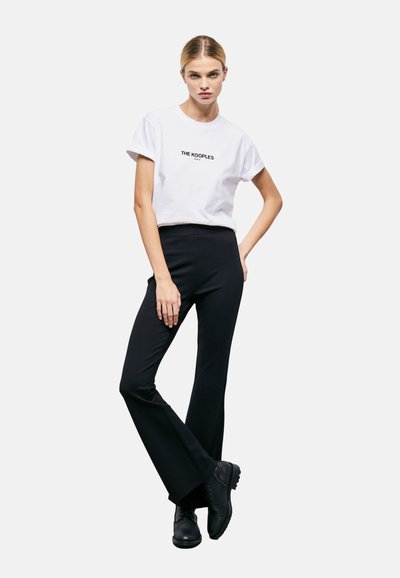 Balta kokvilnas T-kreklu ar sarullētām piedurknēm un melnu logotipu "THE KOOPLES". Melni pieguļoši bikses un masīvas melnas zābakus. Vienkāršs, mūsdienīgs dizains.