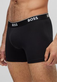 Schwarze Baumwoll-Boxershorts mit einer enganliegenden Passform, ausgestattet mit einem weißen "BOSS"-Logo auf dem elastischen Bund und einer glatten Textur.