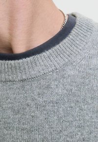 Pull en tricot gris avec un col rond à côtes. Présente un col intérieur bleu foncé et un tissu texturé sur l'ensemble.
