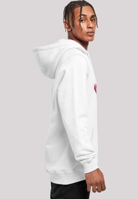 Sudadera blanca hecha de material suave, con un gran bolsillo frontal, puños acanalados y un colorido patrón geométrico en el pecho.