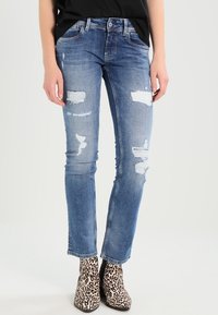 Sininen farkkuhaalari, jossa on kulutuspisteitä, istuva malli ja kapeat lahkeet. Yhdistetty leopardikuvioisiin nilkkabootseihin.