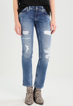 Jeans de mezclilla azul con parches desgastados, un diseño ajustado y pierna tapered. Combinados con botines de estampado de leopardo.