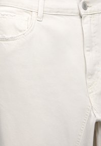 Vitt denimtyg med en subtil diagonals struktur, med klassisk fem-ficksdesign och synliga sömnadsdetaljer längs sömmarna.