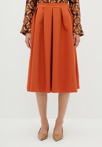 Rust-orange midi kjol med veck, gjord av slätt tyg. Har hög midja och når under knäna, kombinerad med beige spetsiga klackar.