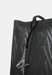 Sac fourre-tout noir texturé avec un motif géométrique, doté d'une sangle noire et d'un charme logo en argent attaché par une chaîne.