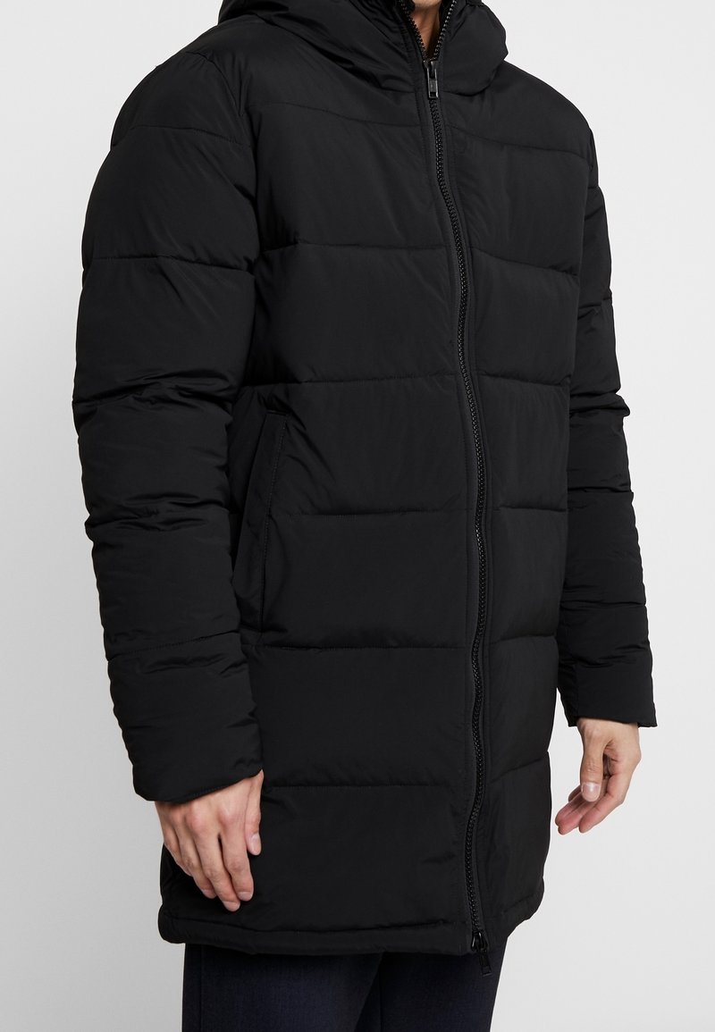 Sort puffjakke med hætte, med lynlås foran og horisontalt quiltet mønster. Blødt, polstret stof med sidelommer.