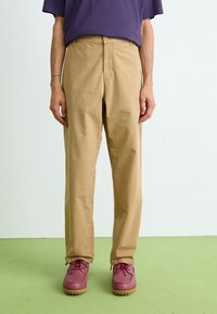Khaki chinos with a straight-leg design, made from a durable fabric. Features front pockets and a button closure, paired with maroon shoes.