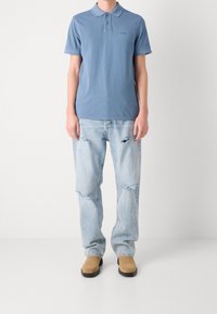 Jasnoniebieska koszulka polo z krótkimi rękawami, z subtelnym logo. Do tego podarte jasnoniebieskie dżinsy oraz beżowe zamszowe botki za kostkę.