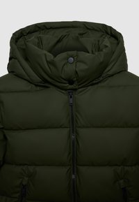 Giacca imbottita verde scuro con colletto alto, zip frontale, bottoni a pressione e tasche laterali con zip su sfondo semplice.